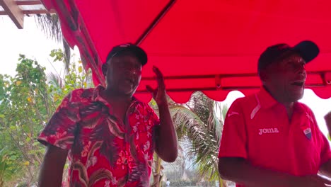 Man-singing-Vallenato-music-while-wearing-a-beach-shirt-along-with-a-man-who-is-playing-the-Guacharaca-on-the-shore-of-Cartagena-de-Indias,-Colombia