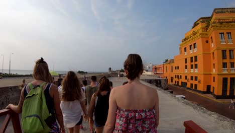 A-group-of-tourists-is-walking-near-an-orange-building-and-stone-wall-of-the-old-town-of-Cartagena-de-Indias,-Colombia