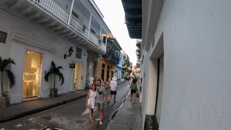 A-couple-of-tourists-are-standing-while-one-person-takes-a-picture-on-a-street-surrounded-by-houses,-stores,-balconies,-doors-and-windows-on-the-old-town-of-Cartagena-de-Indias,-Colombia