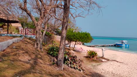 A-paradisiac-island-with-white-sand,-turquoise-ocean-water,-trees-and-small-straw-huts-near-the-shore
