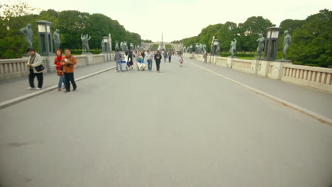 Visitors-and-tourists-cross-a-bridge-in-Frogner-Park,-Oslo,-Norway,-lined-with-statues-from-famous-sculptor-Gustav-Vigeland