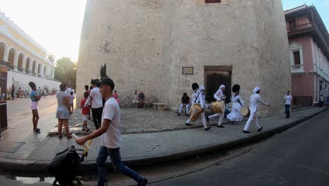 A-group-of-local-people-with-drums-and-white-dresses-are-walking-on-the-street-of-the-old-town-of-Cartagena-de-Indias,-Colombia