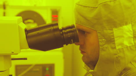 Close-shot-of-male-researcher-in-full-medical-suit-working-in-laboratory-looking-through-microscope