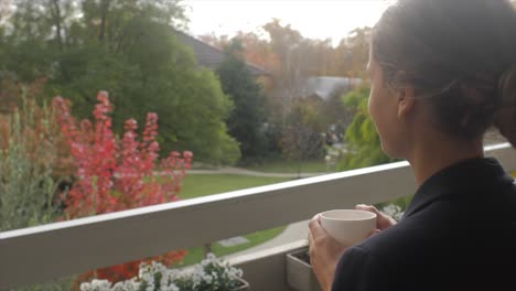 Young-lady-on-balcony-sipping-tea-looking-out-to-beautiful-garden