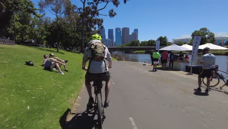 Cyclist-riding-past-people-enjoying-a-beautiful-day-along-side-a-river