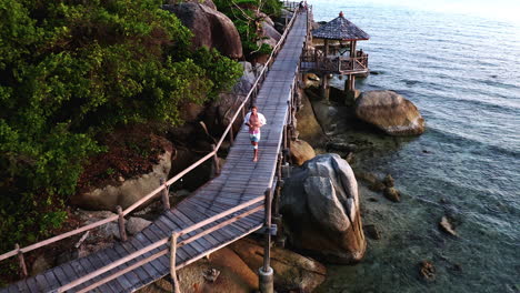 Man-in-unbuttoned-shirt-jogging-on-wooden-boardwalk-along-sea-cliffs