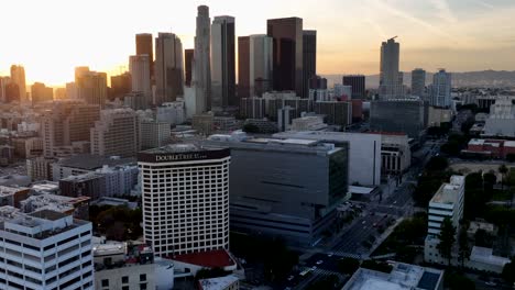 Aerial-view-over-the-city-of-Los-Angeles-downtown-skyline-during-sunset,-flying-past-Double-tree-Hilton-hotel