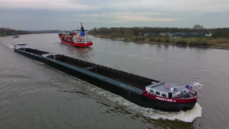 Empty-long-and-thin-cargo-ship-navigating-through-the-inland-canal-of-Zwijndrecht-while-a-fully-loaded-cargo-ship-navigates-to-the-other-side