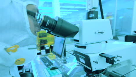 Biólogo-Asiático-Trabajando-Con-Microscopio-En-Laboratorio-Con-Luces-Azules