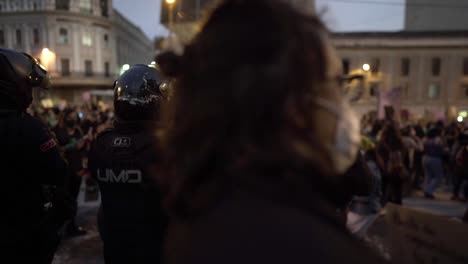 Eine-Frau-Springt-Und-Singt-Auf-Dem-Rücken-Von-Polizisten,-Die-Vor-Einer-Gruppe-Von-Frauen-Stehen,-Die-Während-Des-Internationalen-Frauentags-In-Quito,-Ecuador,-Marschieren