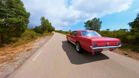 FPV-aerial-following-a-vintage-red-Mustang-along-a-scenic-country-highway-through-the-hills-of-Spain