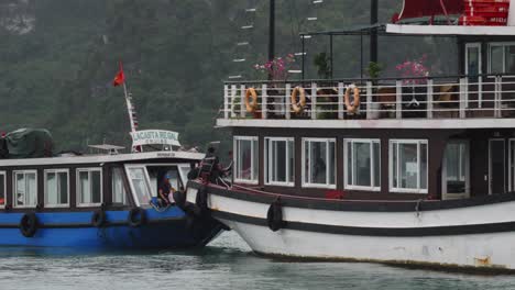 Tracking-shot-of-people-disembarking-from-a-small-ferry-onto-a-tourist-cruise-ship-at-Ha-Long-Bay,-Vietnam