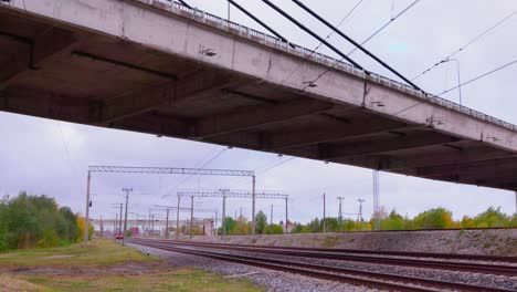passenger-train-rides-under-the-bridge,-railway-construction-train-in-the-background,-wide-shot,-camera-pan