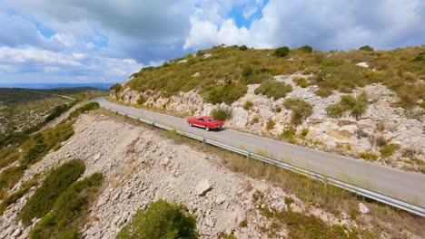 FPV-Luftaufnahme-Eines-Klassischen-Roten-Mustangs,-Der-Eine-Malerische-Bergstraße-Entlang-Fährt