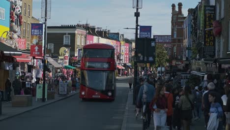 Roter-Doppeldeckerbus-Fährt-Auf-Der-Hauptstraße-In-Camden-Town,-London,-Mit-Einer-Menge-Fußgänger,-Die-Tagsüber-Auf-Gehwegen-Laufen
