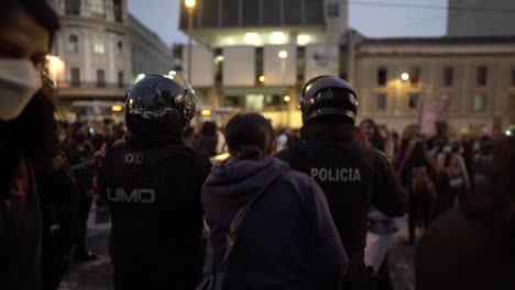 Una-Mujer-Salta-Y-Canta-Junto-A-Policías-Que-Están-Parados-Frente-A-Un-Grupo-De-Mujeres-Que-Marchan-Durante-Una-Protesta-En-El-Día-Internacional-De-La-Mujer-En-Quito,-Ecuador.