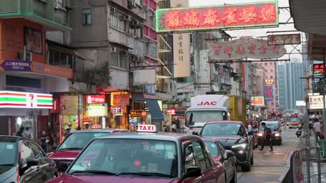 Los-Vehículos-Esperan-En-Un-Semáforo-Encima-De-Ellos,-Hay-Un-Letrero-De-Neón-Comercial-Colgado-De-La-Fachada-De-Un-Edificio-Residencial-En-Hong-Kong