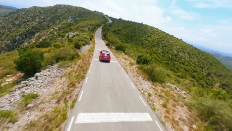 FPV-Seguimiento-Aéreo-De-Una-Camioneta-Roja-Conduciendo-A-Través-De-Un-Pintoresco-Paisaje-Montañoso