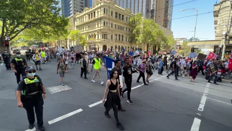 Protesters-holding-signs-rally-in-Melbourne-Australia-walking-down-Collins-Street-stopping-all-traffic,-police-escorting-the-protesters