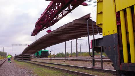Grúa-De-Construcción-Ferroviaria-Descargando-Nueva-Vía-De-Tren,-Los-Trabajadores-Ayudan