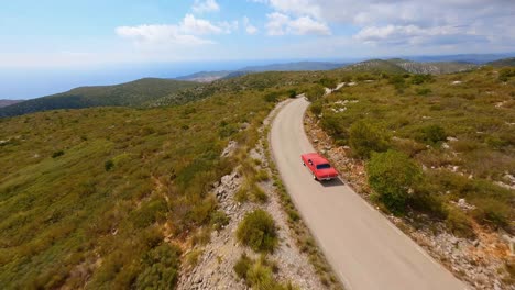 Filmische-FPV-Luftaufnahme,-Die-Einem-Roten-Mustang-Durch-Eine-Malerische-Berglandschaft-Folgt