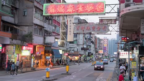 Pedestrians-walk-across-the-street-as-neon-signs-hang-above-the-street