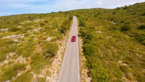 Antena-Fpv-Volando-Detrás-De-Un-Coche-Rojo-Viajando-Por-Una-Carretera-Pintoresca-En-El-Campo-Español