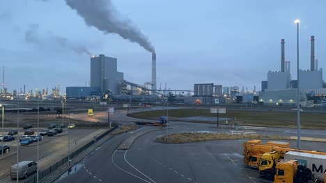 Timelapse-Del-Tráfico-Con-Humo-Saliendo-De-La-Chimenea-De-Una-Planta-Industrial-En-Maasvlakte,-Rotterdam,-Países-Bajos