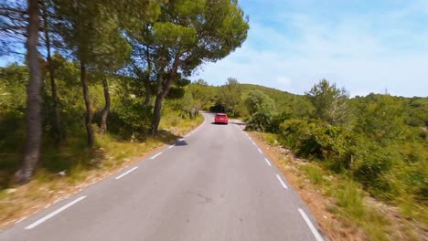 Malerische-FPV-Antenne,-Die-Einem-Roten-Auto-Folgt,-Das-Durch-Die-Malerische-Berglandschaft-In-Spanien-Fährt
