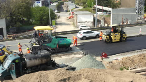 Arbeiter-Asphaltieren-Die-Straße-Mit-Dampfwalze-Und-Straßenfertiger-Neben-Dem-Autoverkehr