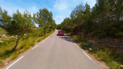 FPV-aerial-following-a-red-car-traveling-along-a-picturesque-country-road-in-the-Spanish-countryside