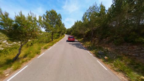 FPV-Antenne,-Die-Einem-Roten-Auto-Folgt,-Das-Auf-Einer-Malerischen-Landstraße-In-Der-Spanischen-Landschaft-Fährt