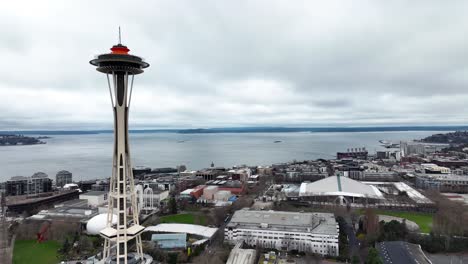 Approaching-Space-Needle-and-Elliott-Bay-in-Seattle-on-an-overcast-cloudy-day,-aerial-drone
