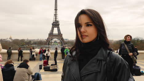 Junges-Brünettes-Mädchen-Berührt-Ihr-Haar-Und-Blickt-In-Die-Kamera-Mit-Blick-Auf-Den-Eiffelturm