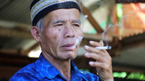 Anciano-Malayo-Fumando-Casualmente-Por-La-Mañana-Frente-A-Su-Jardín