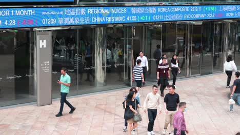 Fußgänger-Gehen-An-Einer-Elektronischen-Tickertafel-Und-Einem-Bildschirm-Vorbei,-Auf-Dem-Börsenzahlen-Vor-Dem-Exchange-Square-Komplex-Angezeigt-Werden,-In-Dem-Sich-Die-Hongkonger-Börse-Befindet