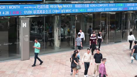 Pedestrians-walk-past-an-electronic-ticker-board-and-screen-displaying-stock-market-figures-outside-the-Exchange-Square-complex,-which-houses-the-Hong-Kong-Stock-Exchange