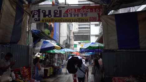 Blick-Auf-Menschen,-Die-An-Regnerischen-Tagen-Regenschirme-Benutzen-Und-Den-Eingang-Des-Lokalen-Marktes-In-Silom-Soi-10,-Bangkok,-Thailand-Verlassen