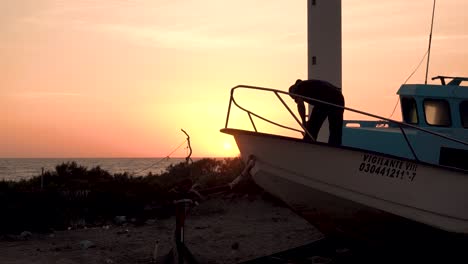 Fisherman-tending-boat-at-sunset-in-front-of-Lighthouse-in-western-Baja,-Medium-shot