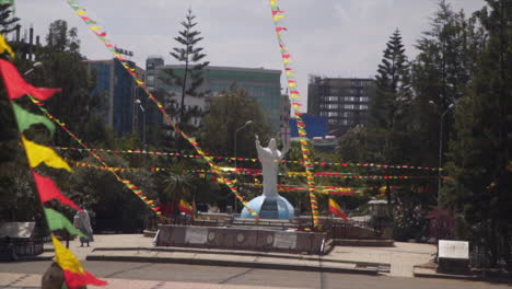 Estatua-Frente-A-La-Catedral-De-La-Santísima-Trinidad-En-Addis-Abeba,-Etiopía,-Con-Banderas-Rojas,-Verdes-Y-Amarillas