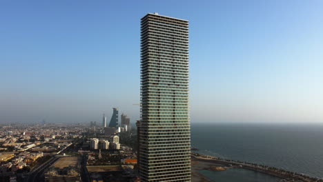 Aerial-view-tilting-toward-the-sunlit-Sail-tower,-in-Jeddah-city,-Saudi-Arabia