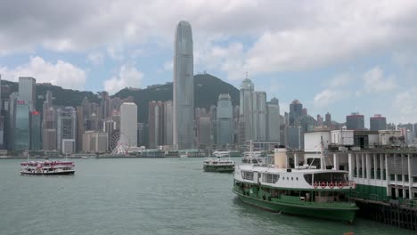Blick-Auf-Den-Seehafenverkehr-Von-Hongkong,-Während-Star-Ferries-Abfahren-Und-Am-Pier-Des-Fährterminals-Am-Wasser-Ankommen,-Während-Im-Hintergrund-Die-Skyline-Von-Hongkong-Zu-Sehen-Ist