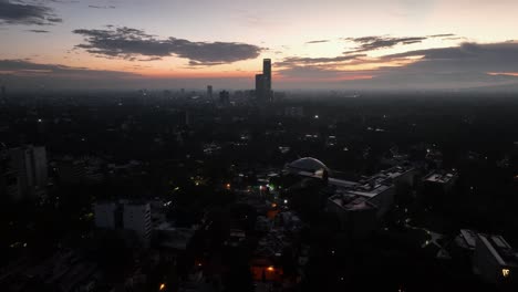 Drone-shot-over-the-cityscape,-toward-the-Mítikah-tower,-hazy-evening-in-Mexico-city