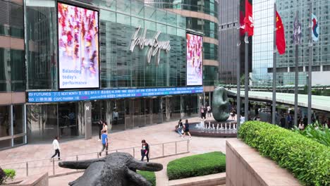 Fußgänger-Gehen-An-Einer-Elektronischen-Tickertafel-Und-Einem-Bildschirm-Vorbei,-Auf-Dem-Börsenzahlen-Vor-Dem-Exchange-Square-Komplex-Angezeigt-Werden,-In-Dem-Sich-Die-Hongkonger-Börse-Befindet