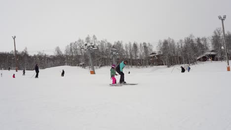 Mother-holding-hand-and-tutoring-young-unexperienced-daughter-in-skiing-slope