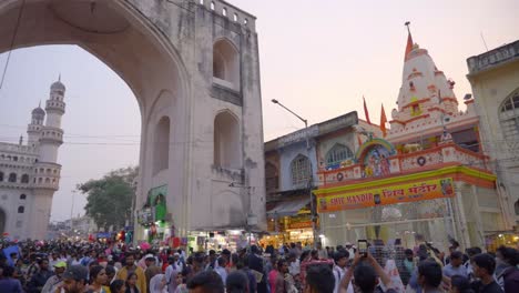 Crowded-and-busy-market-of-old-Hyderabad-with-people-walking-across-the-streets-with-famous-and-historical-Charminar-in-view-,-India