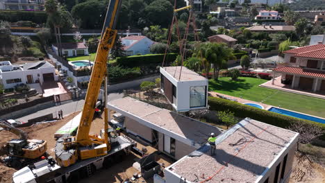 Workers-building-expensive-modular-home-with-crane,-aerial-orbit-view