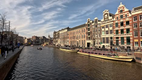 A-tour-group-traveling-down-the-Rokin-canal-on-a-sightseeing-tour,-the-cruise-boat-passing-the-beautiful-traditional-Dutch-buildings-along-the-river,-Amsterdam,-Netherlands