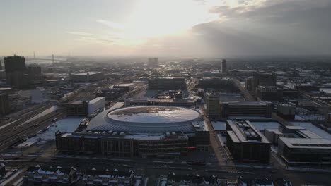 Snowstorm-rolling-over-downtown-Detroit-with-massive-arena,-aerial-view