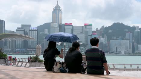 Junge-Touristen-Sitzen-Am-Ufer-Von-Victoria-Und-Genießen-Den-Blick-Auf-Den-Hafen-Und-Die-Skyline-Von-Hongkong